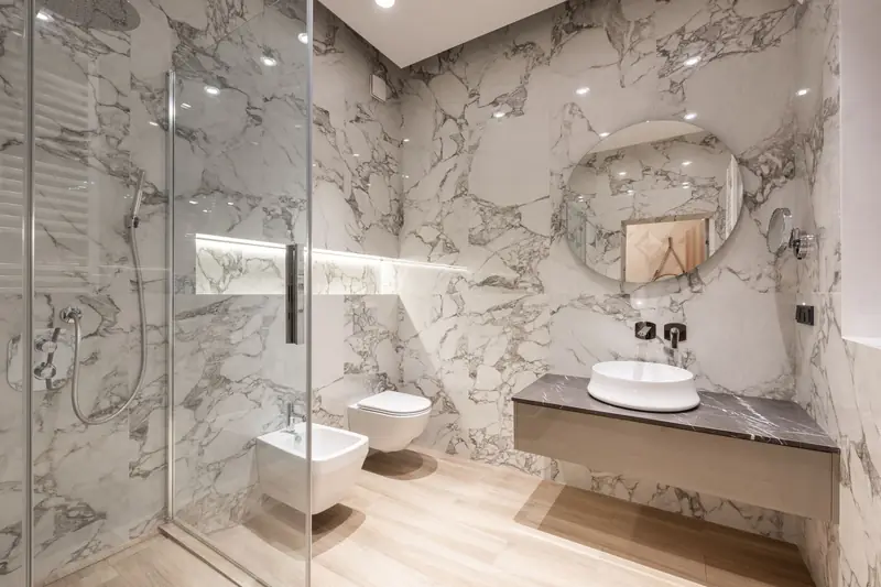 A marble bathroom with a walk-in shower, wall-hung fixtures and a timber floor.