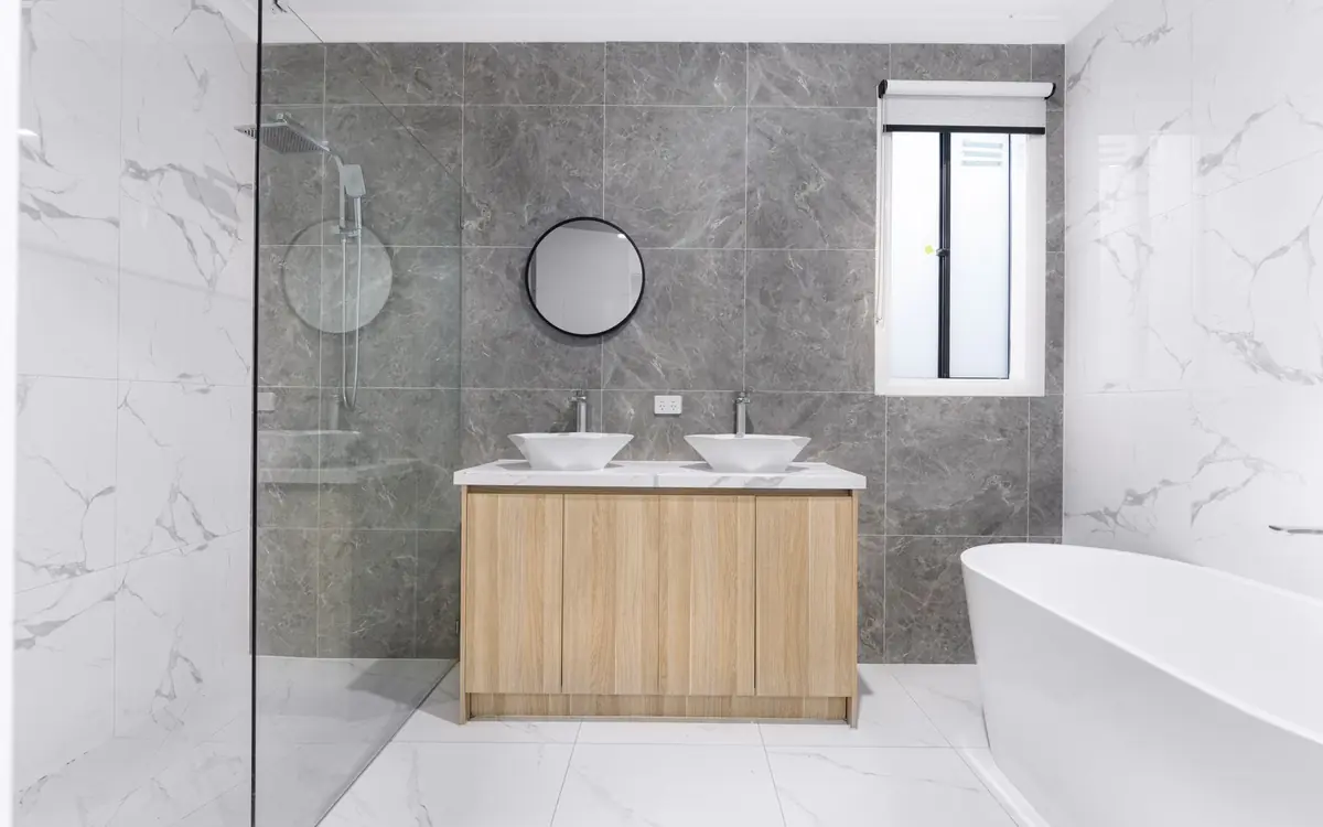 A finished bathroom in grey marble tile with a timber vanity, twin basins and a freestanding tub.