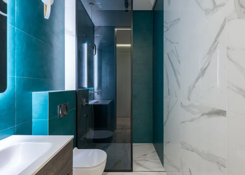 A bathroom with teal tiling, a glass shower screen and a wall-hung toilet.