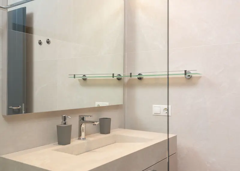 A stone vanity with an integrated basin, chrome mixer and a full-width mirror.