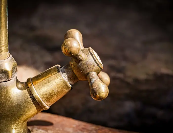A brass bibcock tap mounted on weathered timber.
