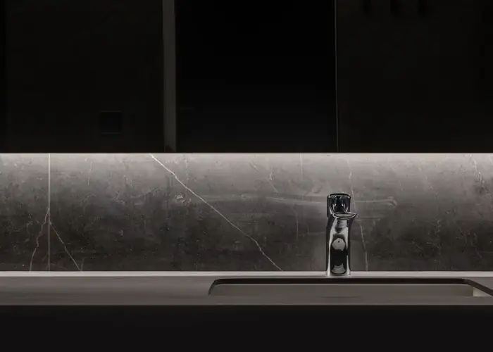 A chrome basin mixer on a dark marble vanity, lit from above.