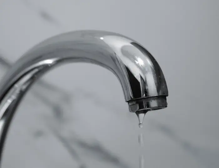 A chrome spout with a single drop of water falling from it.