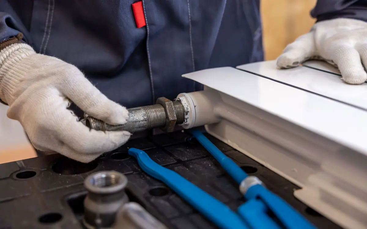 Gloved hands fitting a threaded pipe nipple, with blue pipe wrenches on the bench.