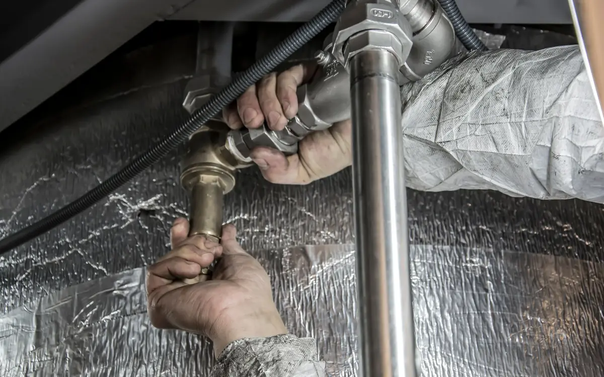A plumber's hands tightening a brass shut-off valve onto a stainless supply line.