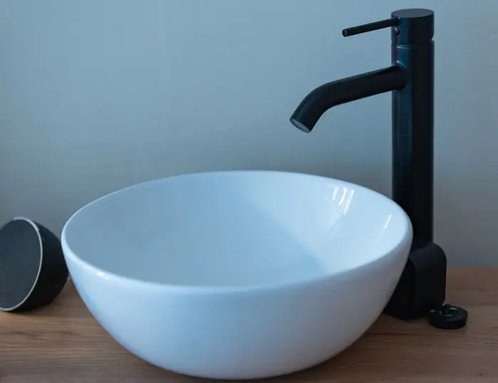 A matte black mixer tap over a pale blue vessel basin on a timber counter.